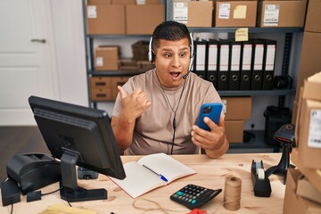 Sticker - Hispanic young man working at small business ecommerce on video call pointing thumb up to the side smiling happy with open mouth