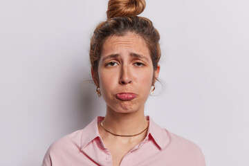 Wall Mural - Portrait of displeased frustrated woman purses lips and looks sadly expresses negative emotions dressed in shirt has depressed facial expression isolated over white background feels sorrowful