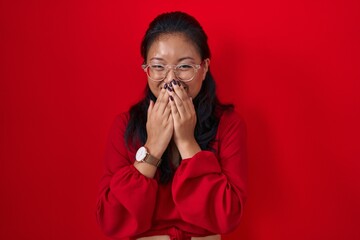 Sticker - Asian young woman standing over red background laughing and embarrassed giggle covering mouth with hands, gossip and scandal concept