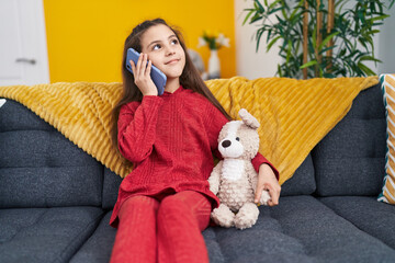 Sticker - Adorable hispanic girl talking on smartphone sitting on sofa at home