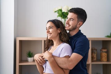 Wall Mural - Young hispanic couple hugging each other standing at home