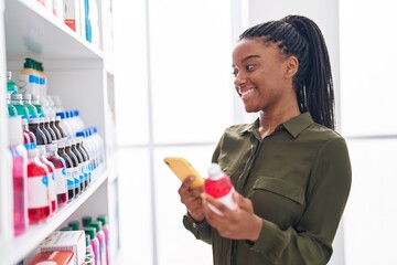 Sticker - African american woman customer using smartphone holding medicine bottle at pharmacy