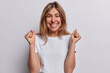 © wayhome.studio  - I am champion. Glad young European woman clenches fists and smiles toothily looks with joy at camera dressed in casual t shirt isolated over white background feels happy after winning or triumph