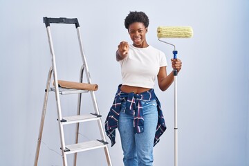 Sticker - African american woman holding roller painter pointing to you and the camera with fingers, smiling positive and cheerful