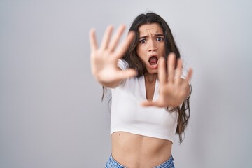 Sticker - Young teenager girl standing over white background afraid and terrified with fear expression stop gesture with hands, shouting in shock. panic concept.