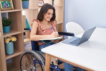Young hispanic woman sitting on wheelchair studying at home