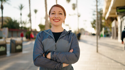 Wall Mural - Young redhead woman wearing sportswear standing with arms crossed gesture at street