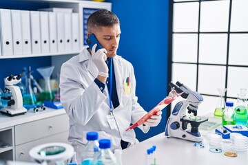 Sticker - Young hispanic man scientist talking on the smartphone reading document at laboratory