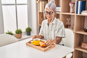 Poster - Middle age grey-haired woman having breakfast sitting on table at home