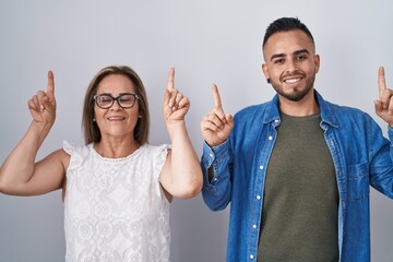 Sticker - Hispanic mother and son standing together smiling amazed and surprised and pointing up with fingers and raised arms.