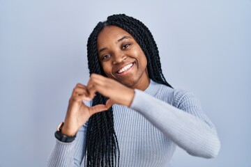 Wall Mural - African american woman standing over blue background smiling in love doing heart symbol shape with hands. romantic concept.