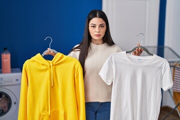 Poster - Young woman hanging clothes on racks relaxed with serious expression on face. simple and natural looking at the camera.