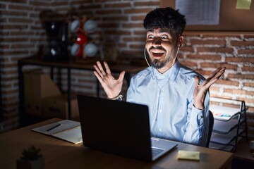 Poster - Young hispanic man with beard working at the office at night celebrating crazy and amazed for success with arms raised and open eyes screaming excited. winner concept