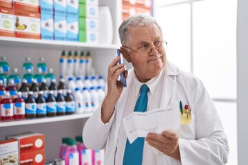 Poster - Middle age grey-haired man pharmacist talking on smartphone reading prescription at pharmacy