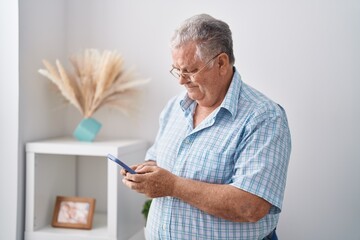 Canvas Print - Middle age grey-haired man using smartphone standing at home