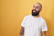 © Krakenimages.com - Young hispanic man with beard and tattoos standing over yellow background looking away to side with smile on face, natural expression. laughing confident.