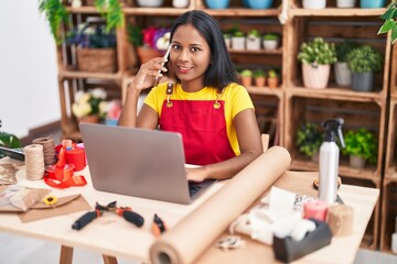 Canvas Print - Young beautiful woman florist talking on smartphone using laptop at florist