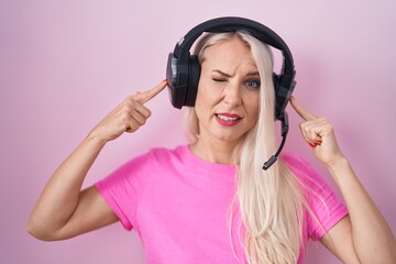 Poster - Caucasian woman listening to music using headphones covering ears with fingers with annoyed expression for the noise of loud music. deaf concept.