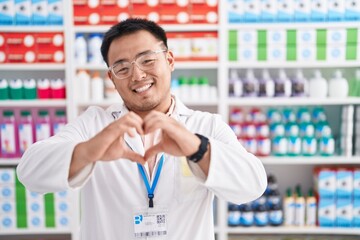 Poster - Chinese young man working at pharmacy drugstore smiling in love doing heart symbol shape with hands. romantic concept.