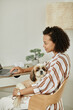 © Seventyfour - Side view portrait of black young woman working from home with pet dog sitting in lap