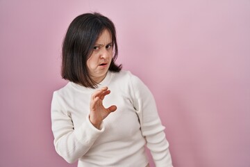 Poster - Woman with down syndrome standing over pink background disgusted expression, displeased and fearful doing disgust face because aversion reaction.