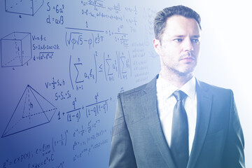 Portrait of attractive young european businessman with mathematical formulas on blue background. Teacher, math, education and research concept.