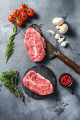 Wall Mural - Top-blade chuck steak on black slate , and meat butcher cleaver marbled beef  with herbs tomatoes peppercorns over grey stone surface background top view.