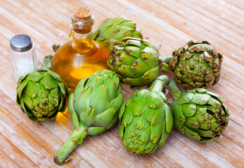 Wall Mural - Bunch of artichokes placed over wooden background with saltcellar and glass oil bottle.