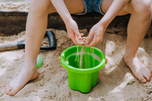 Girl, A Child Is Playing With Sand While Sitting In A Sandbox With A Bucket. Close-up Photography, Portrait, Childhood.