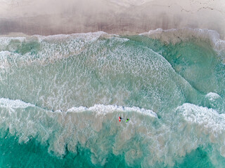 Wall Mural - Aerial drone view of two colourful surfers in the surf at the beach. Clear blue sea water in the summer sunshine.