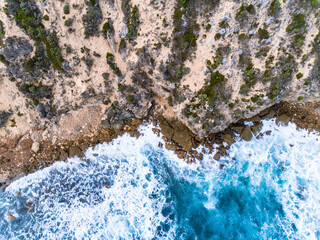 Wall Mural - Aerial top down view of rocky cliffs and clear blue water. Ocean waves smashing on the cliffs as a background. Beautiful natural winter vacation holidays background. Margaret River, Western Australia.