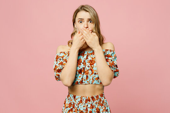 Young shocked surprised scared blonde caucasian woman wear summer casual clothes look camera cover mouth with hands isolated on plain pastel light pink background studio portrait. Lifestyle concept.