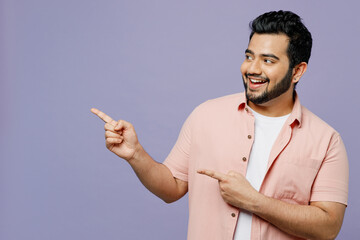 Wall Mural - Young Indian man wear pink shirt white t-shirt casual clothes point index finger aside indicate on workspace area copy space mock up isolated on plain pastel light purple background studio portrait.