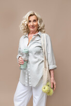 Senior Businesswoman With Mesh Bag And Water Bottle Against Beige Background