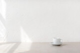 Fototapeta Kawa jest smaczna - Minimalist nordic style good morning concept, cup with drink on beige table and empty white wall with aesthetic natural sunlight shadows and copy space
