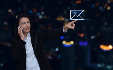 Businesswoman hand pressing email icon over blur colorful night light modern city tower and skyscraper, Business contact us online concept