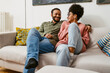 © Drobot Dean - Cheerful multiethnic couple hugging while sitting on couch at home