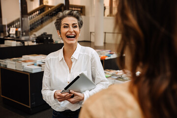 Cheerful mature woman art gallery manager holding tablet and talking to someone while working in museum shop