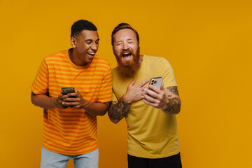 Wall Mural - Two excited men laughing while looking at phone screen standing isolated