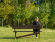 Samotna młoda kobieta blondynka siedzi na długiej ławce w parku, patrząc w dal, z tyłu 