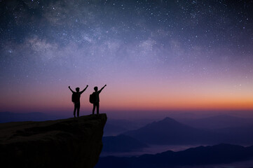 Wall Mural - Silhouette of couple young traveler and backpacker watched the star and milky way alone on top of the mountain. He enjoyed traveling and was successful when he reached the summit.
