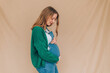 profile portrait of happy pregnant woman touching her belly satisfied - blond caucasian woman in dungarees