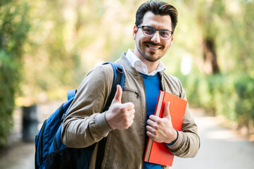 Male student outdoor smiling in a college park giving thumbs up