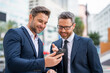 © Volodymyr - Two business men using mobile phone app texting outside of office in urban city. Businessmen holding smartphone for business work. Successful business man typing on smartphone outdoor.