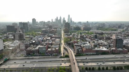 Wall Mural - Aerial descent towards Philadelphia at sunset. Skyline in distance with sunny overexposed sky. Drone establishing shot. Highway in foreground with city traffic.
