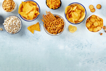 Wall Mural - Salty snacks, party mix, overhead flat lay shot with copy space. An assortment of appetizers on a slate background. Potato and tortilla chips, crackers, popcorn etc