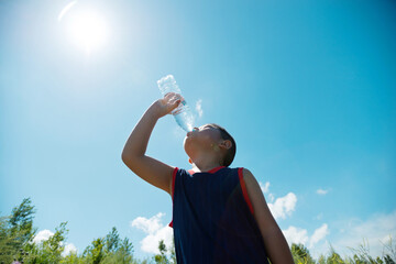 Little asian boy drinking water against blue sky