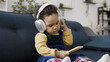 © Synthex - Sweet little baby pretends to listen to music while holding a smartphone and wearing large headphones