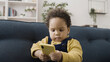 © Synthex - Curious African American baby playing with parent's smartphone, looking bossy