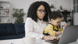© Synthex - Black businesswoman is doing her job on her laptop while babysitting her little son, juggling responsibilities